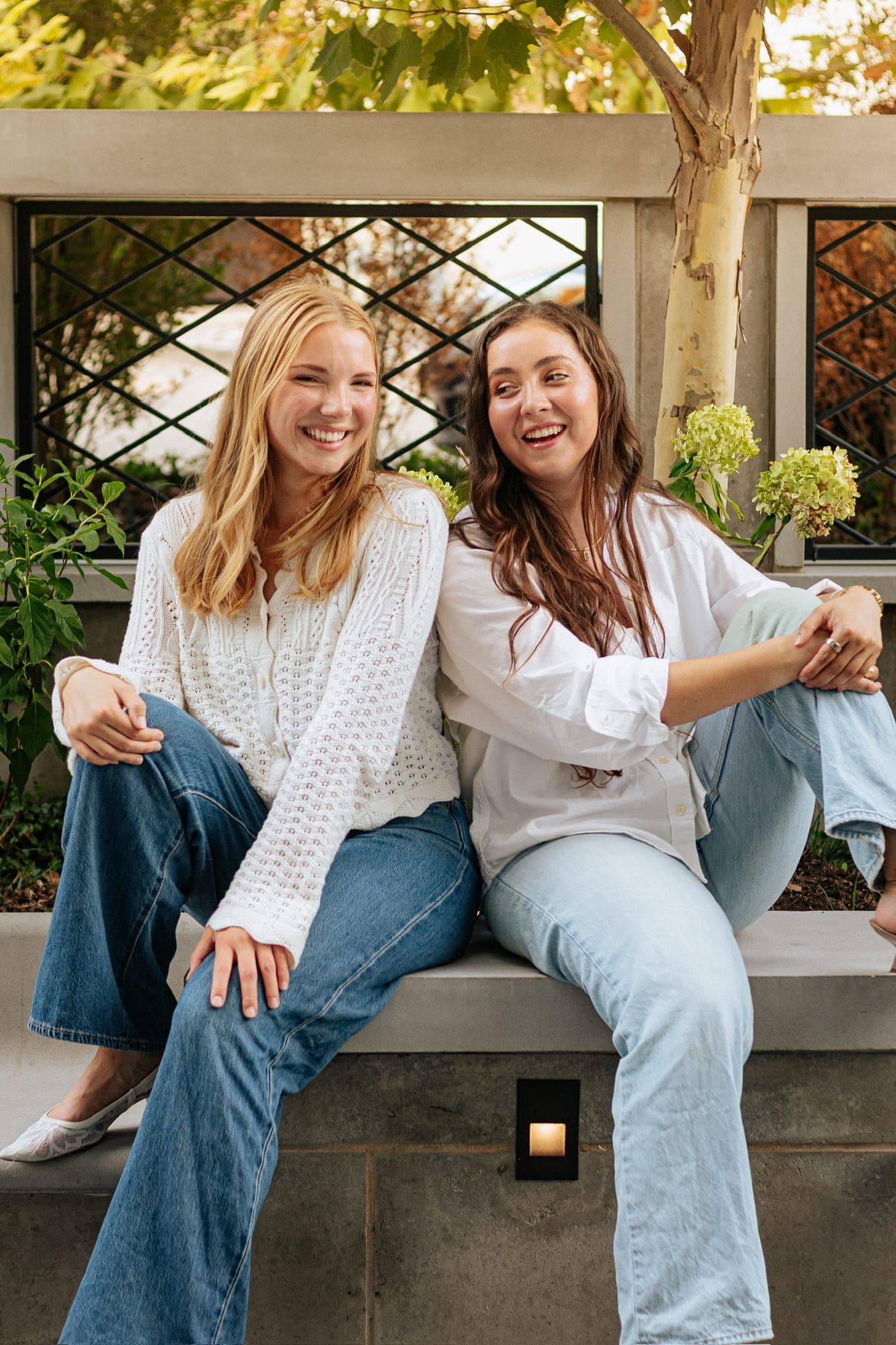 Maddie (left) and Lindsay (right), the founders of Petal Punch, sitting side by side on a bench and laughing